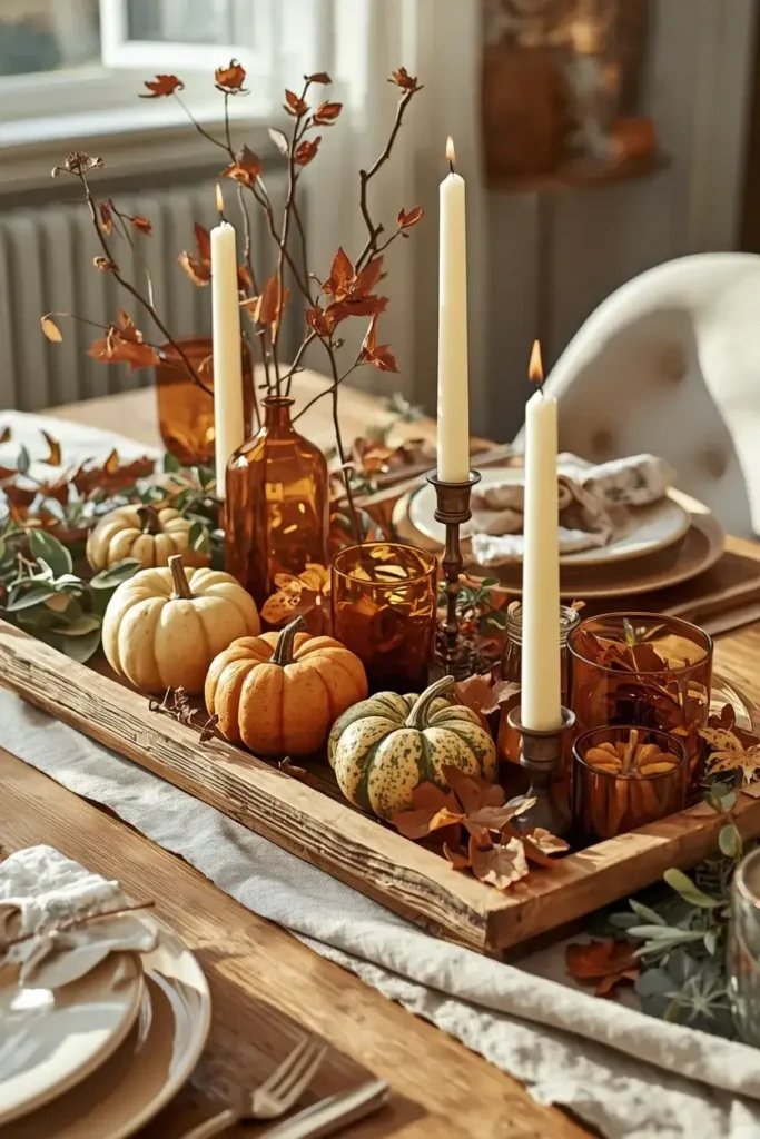 Cozy seasonal table centerpiece with pumpkins, dried leaves, branches, and warm candles.