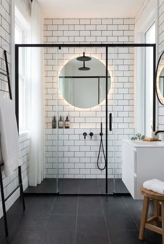Modern bathroom with black framed glass shower doors, white tile walls, and matte black fixtures.