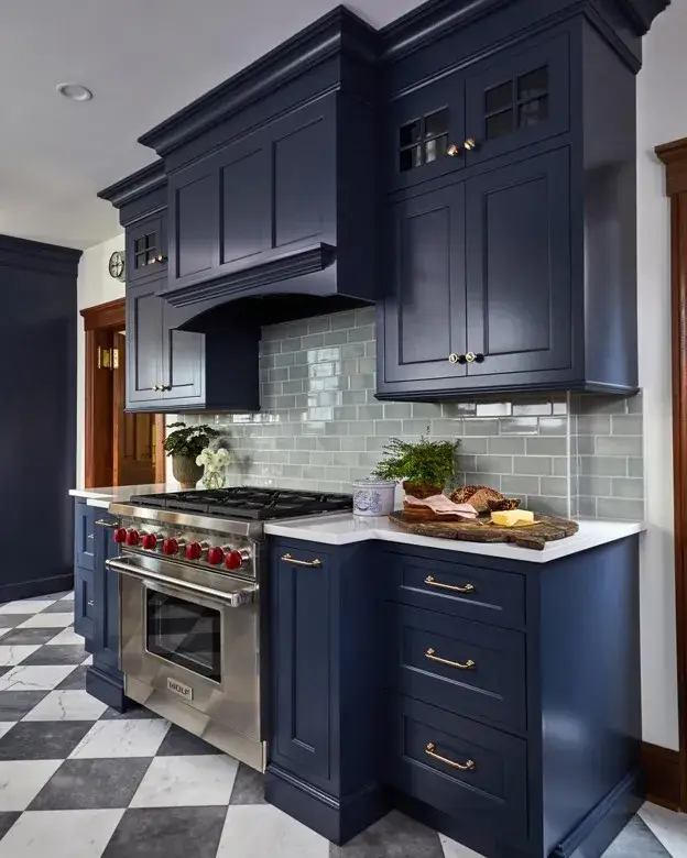 Navy kitchen cabinets with a blue and white tiled backsplash, white countertops, and brass hardware.