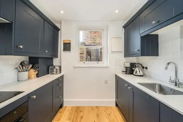 Small kitchen with dark blue cabinets, white countertops, light backsplash, and practical storage.