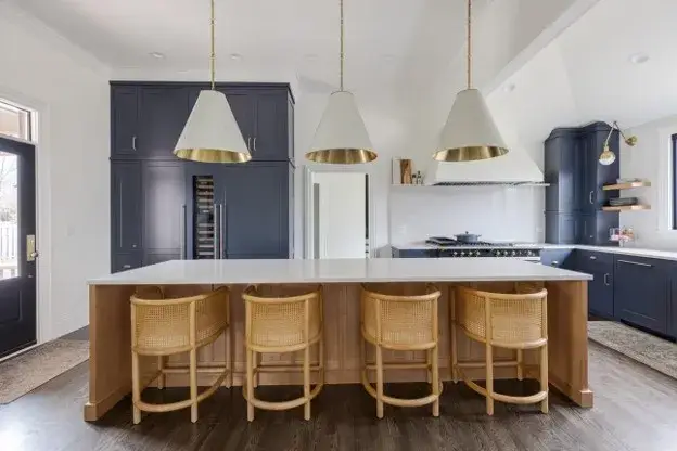 : Dark blue kitchen cabinets with white marble countertops, a warm wood island, brass hardware, and pendant lighting.