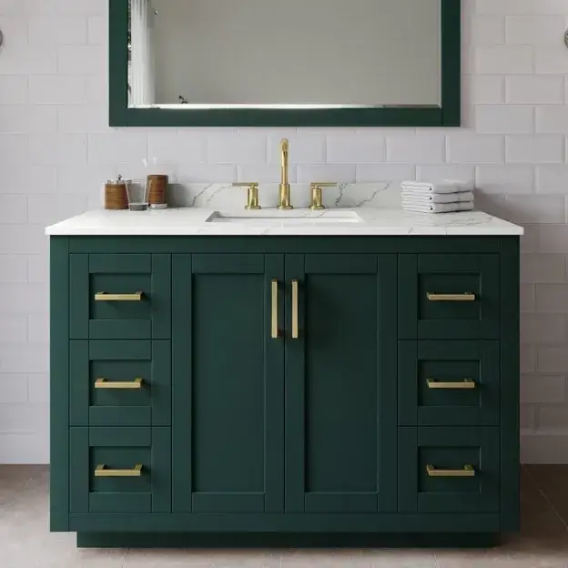 Dark green bathroom cabinet with brass handles, white marble countertop, and elegant gold mirror.