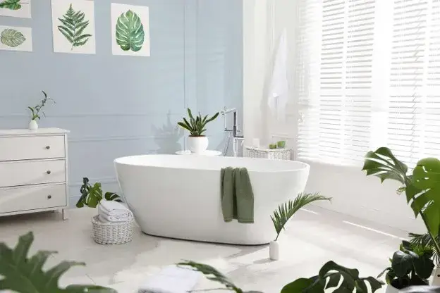 Light blue bathroom with lush green plants, white bathtub, natural wood accessories, ceramic pots, and a relaxing spa-inspired atmosphere.