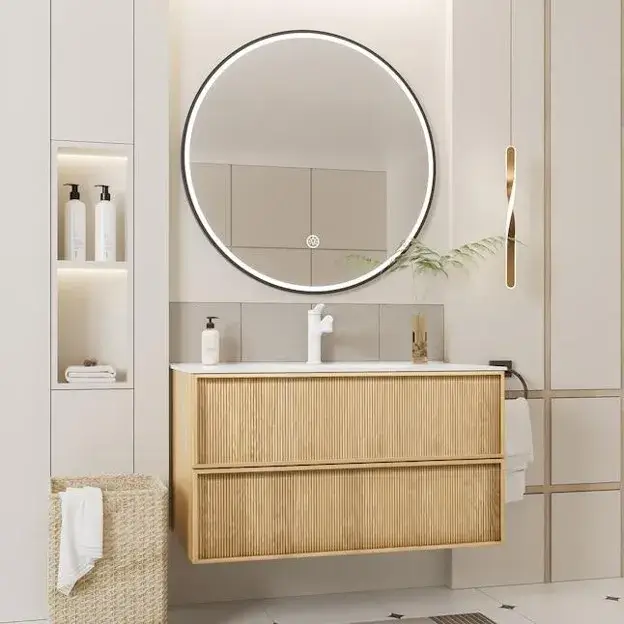 Modern floating oak bathroom cabinet with a white countertop, round mirror, brass fixtures, and warm lighting.